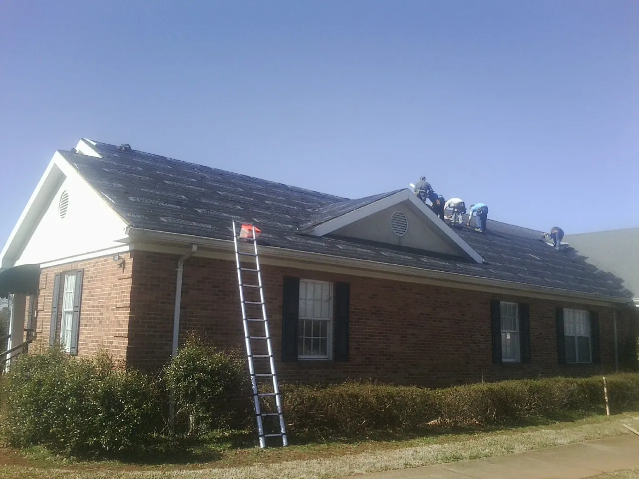 Crew tearing shingles off a brick ranch roof with a ladder set — Metal Roof Repair work by our crew in Mount Croghan