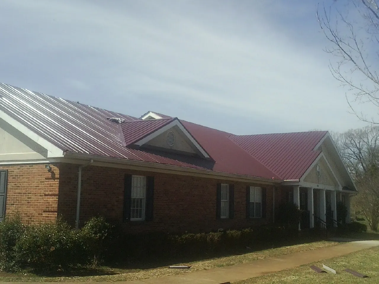 Red metal roof with gabled entries on a long brick building, from a Hail Damage Roof Repair job in Mount Croghan