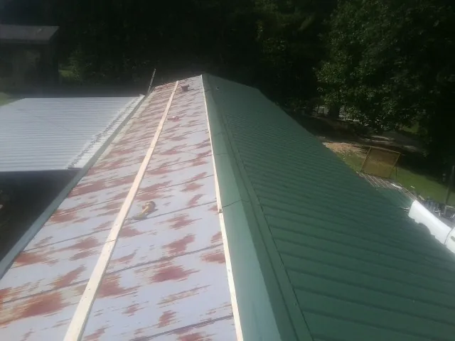 Old rusted panels beside newly installed green metal roofing — Wind Damage Roof Repair by Roofing Brothers in Mount Croghan
