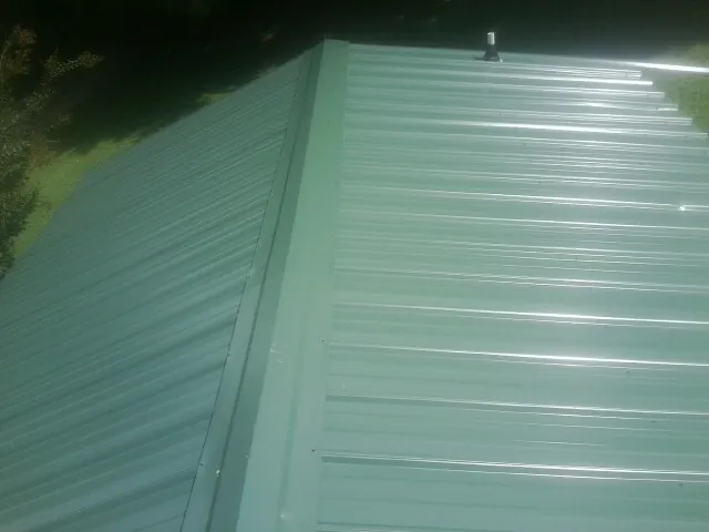 New green metal panels meeting at the ridge of a roof — Flat Roof Repair work by our crew in Mount Croghan