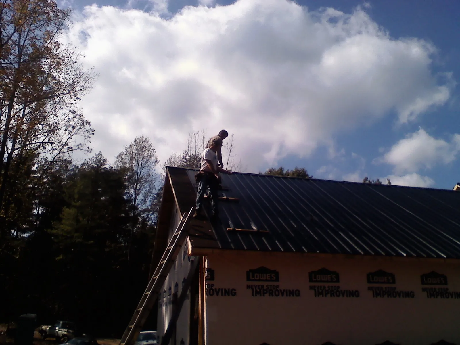 Roofer fastening dark metal panels high against a cloudy sky, from a Roof Inspection job in Mount Croghan