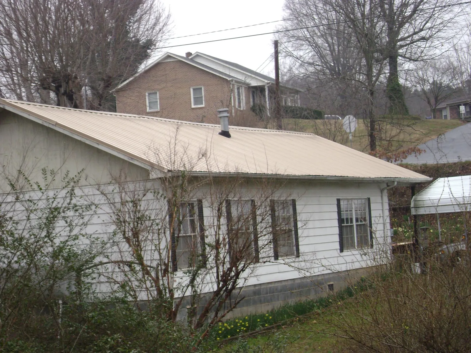 Tan metal roof on a white sided house set into a hillside — Commercial Roofing by Roofing Brothers in Mount Croghan