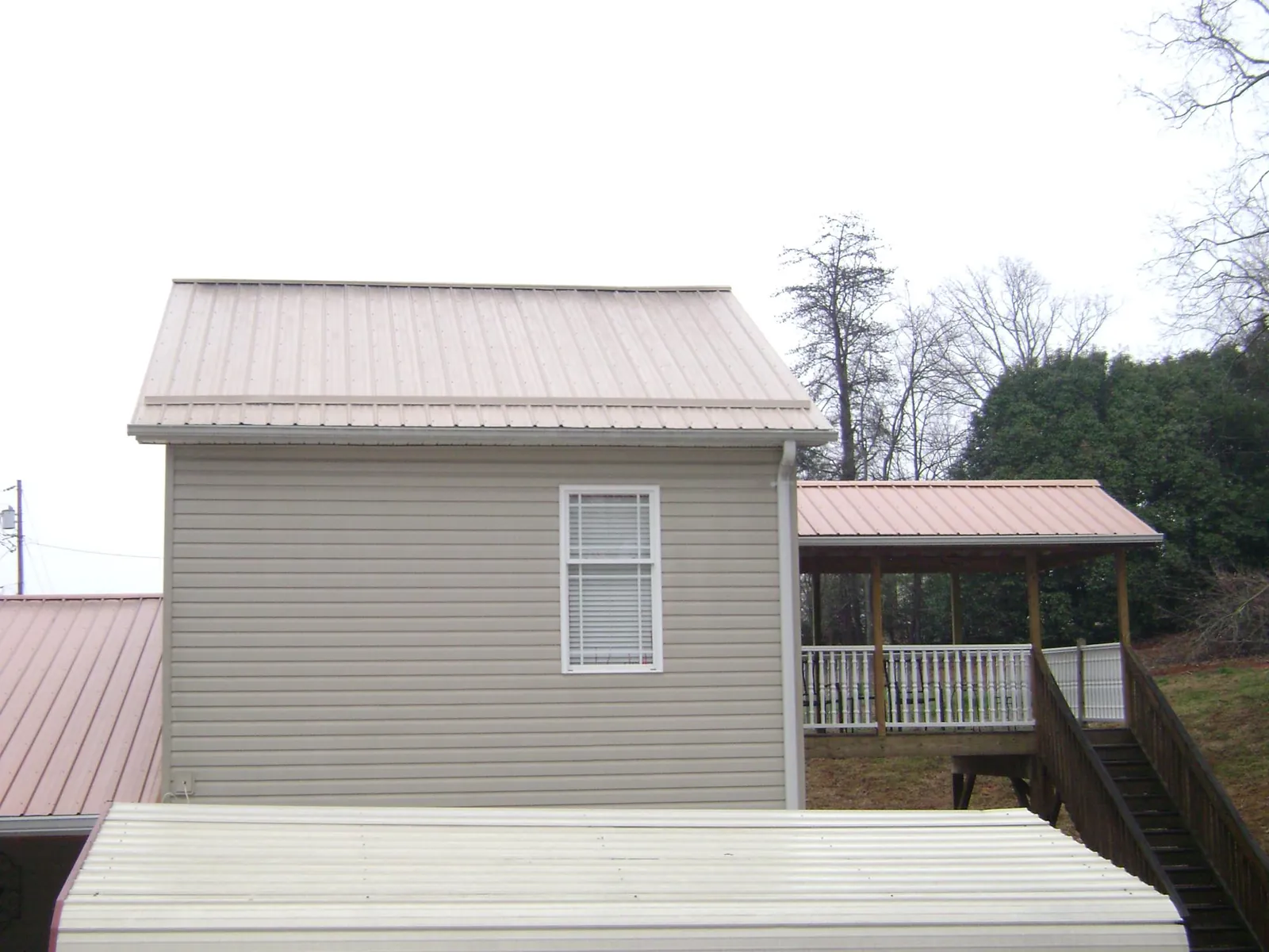 Tan metal roofs on a two story addition and attached porch, from a Roof Replacement job in Mount Croghan